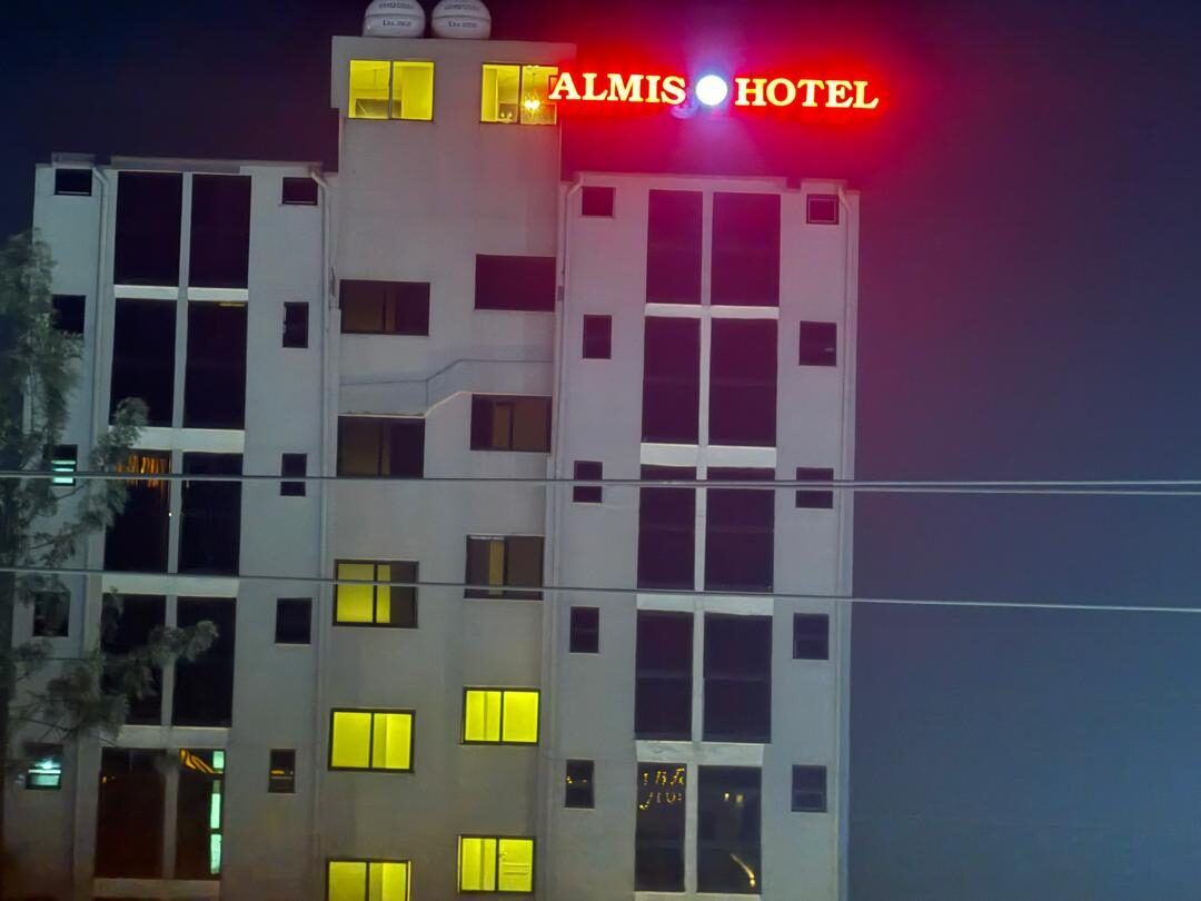 Almis Hotel at night, a white six-storey building with the red ALMIS HOTEL sign lit on the roof
