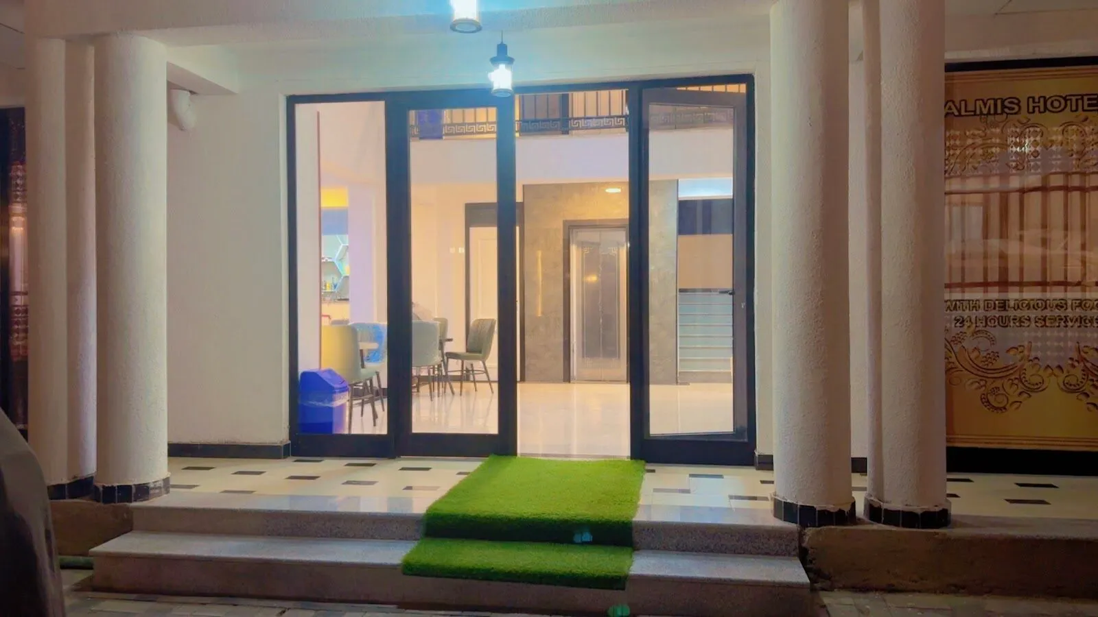 Glass entrance doors of the hotel at night, with the bright lobby and lift visible inside