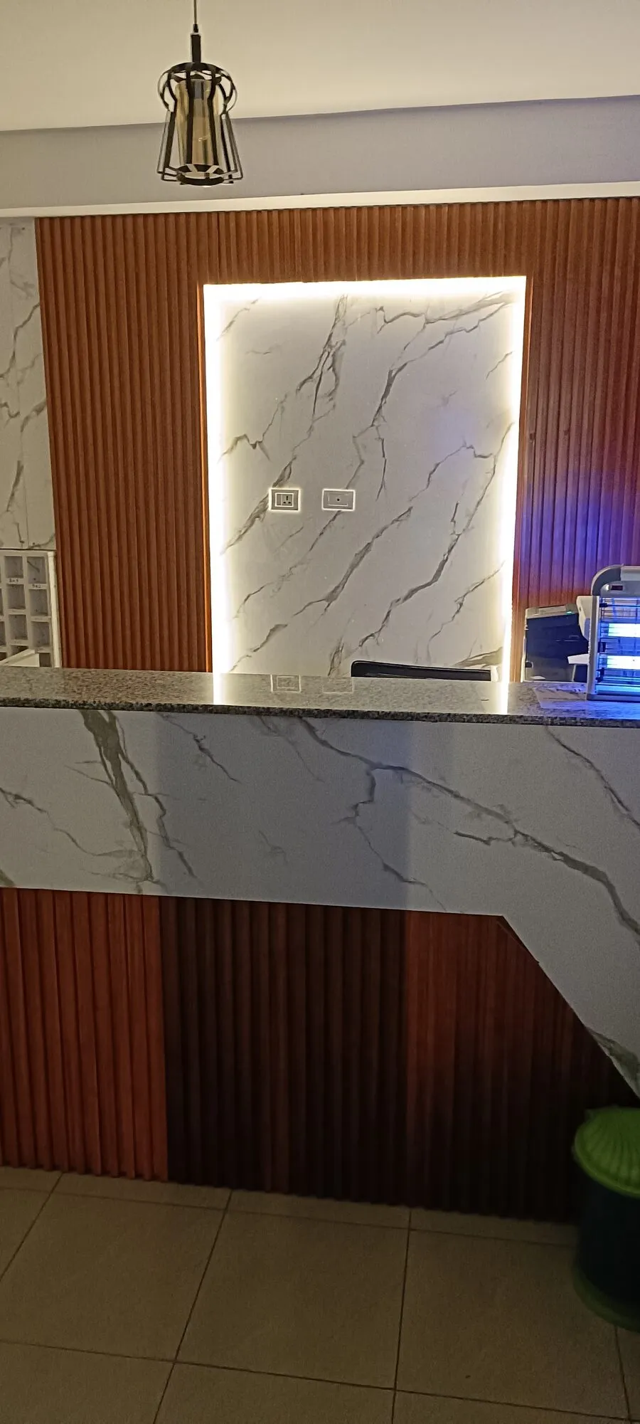 Reception desk in white marble with grey veining, backlit, set against wooden slat panels