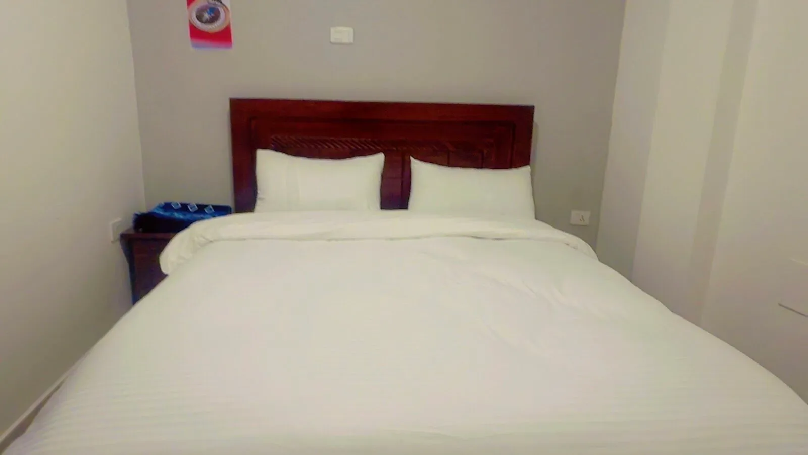 Double room with two pillows on a wide white bed against a mahogany headboard